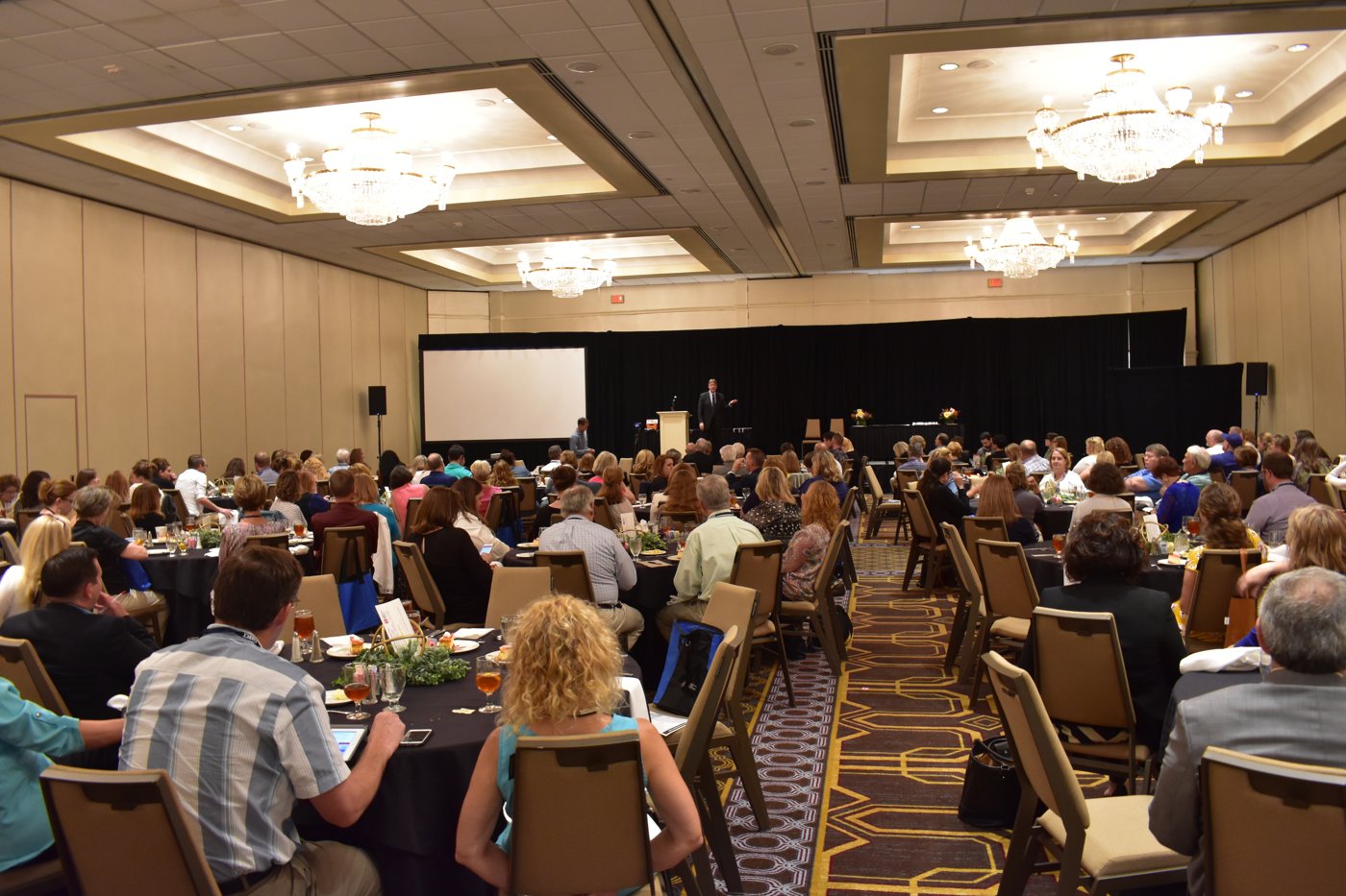 Attendees seated at round tables in a hotel ballroom listening to a keynote speaker at a UMSI training event