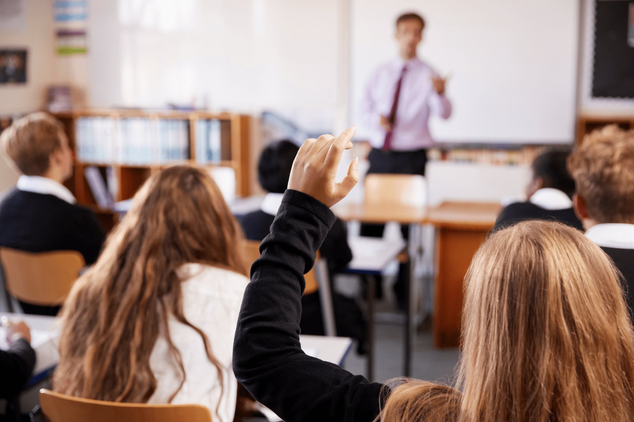 A student raises her hand in a University-Model® school classroom while the teacher leads a lesson