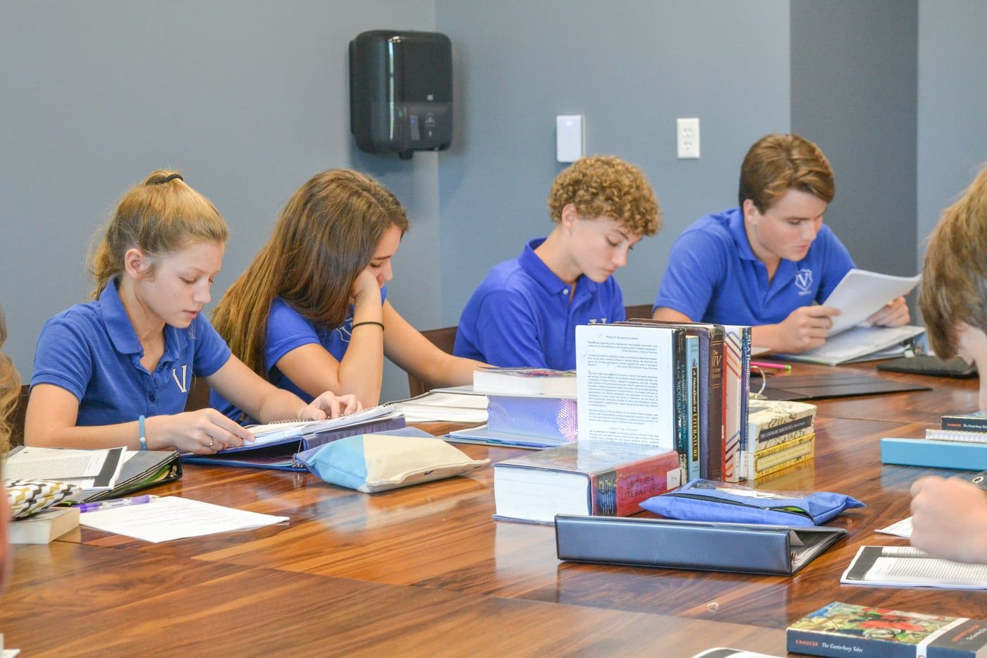 Uniformed students at a member school studying together around a seminar table stacked with literature books