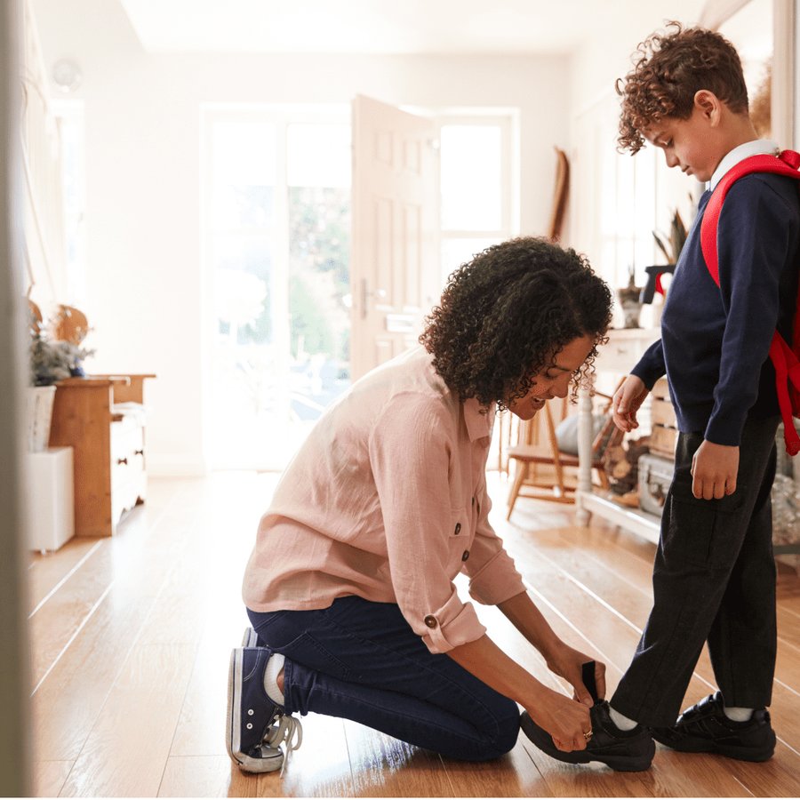 A mother sits beside her son at home, helping him work through his schoolwork