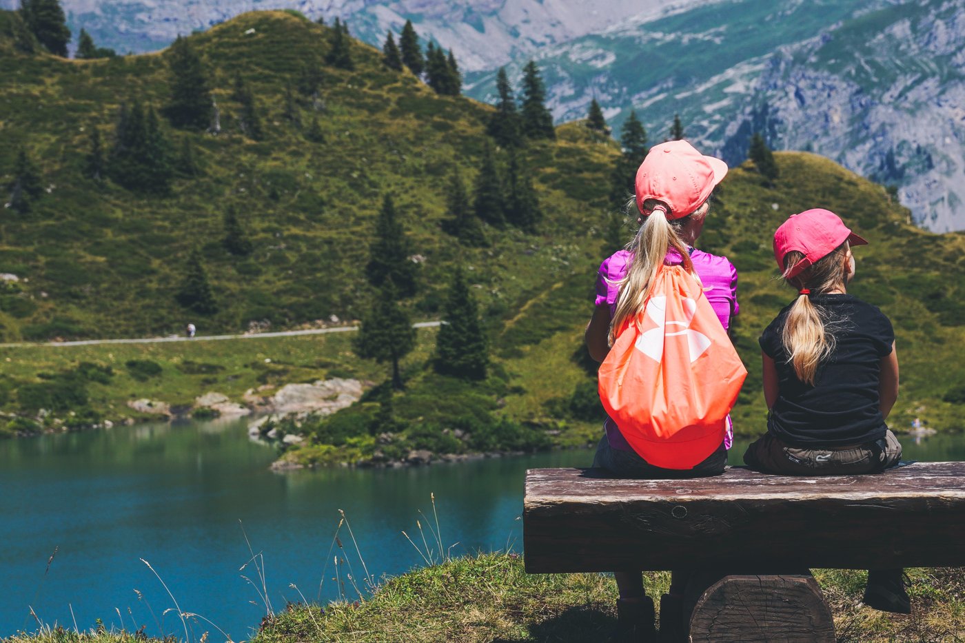Two students with backpacks sit on a wooden bench above a mountain lake, taking in the view on a day outside the classroom.